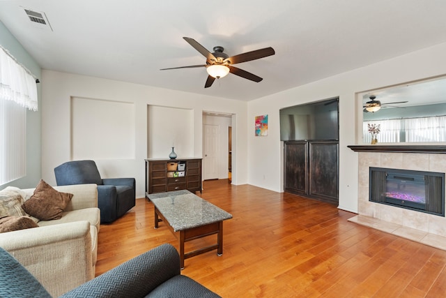 living room featuring hardwood / wood-style flooring, a tile fireplace, and ceiling fan