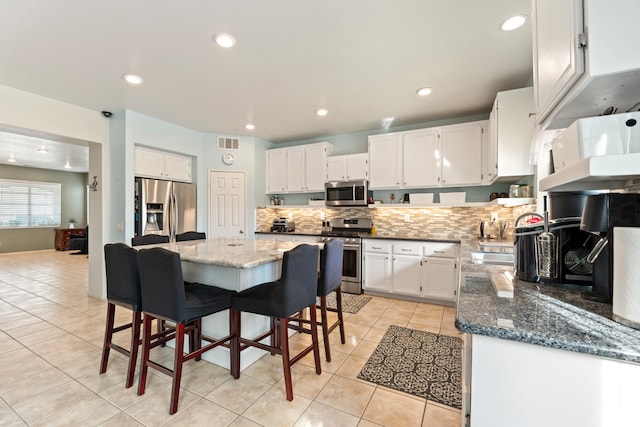 kitchen with appliances with stainless steel finishes, light tile patterned floors, decorative backsplash, white cabinets, and dark stone countertops