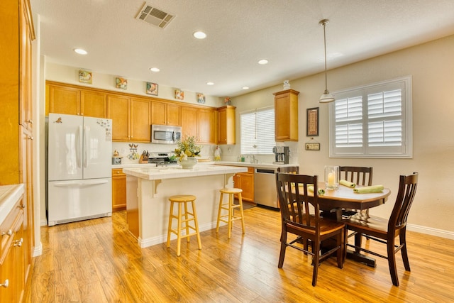 3216 Janine Ave, Rosamond, CA 93560 - kitchen with stainless steel appliances, a kitchen island, a breakfast bar area, light wood-style flooring, and brown cabinets