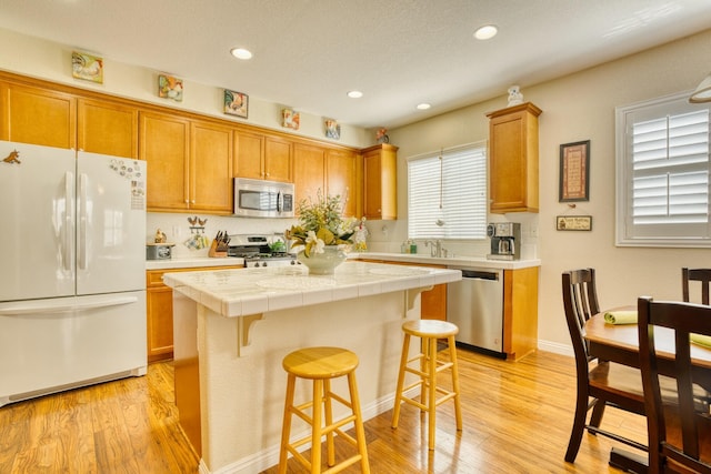 3216 Janine Ave, Rosamond, CA 93560 - kitchen featuring stainless steel appliances, tile counters, a kitchen island, brown cabinets, and light wood-style flooring