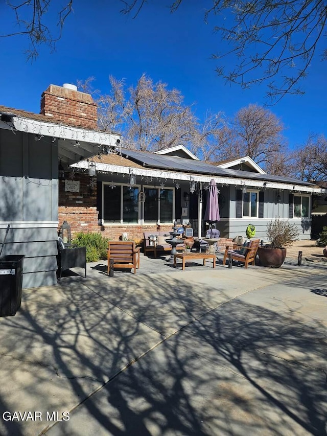 1283 W Lancaster Blvd, Lancaster, CA 93534 - rear view of house featuring a chimney, solar panels, a patio, an outdoor hangout area, and brick siding