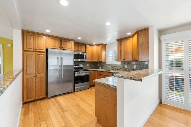 kitchen featuring light wood finished floors, appliances with stainless steel finishes, brown cabinets, a peninsula, and a sink