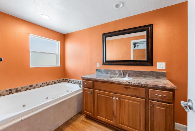 bathroom with a tub with jets, wood finished floors, and vanity