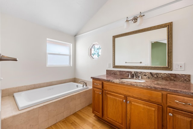 bathroom with lofted ceiling, a garden tub, wood finished floors, and vanity