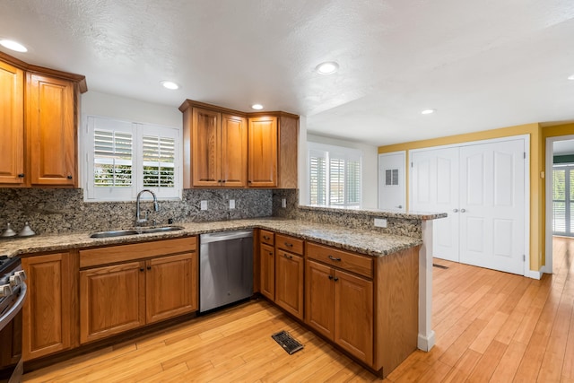 kitchen featuring brown cabinets, a peninsula, stainless steel appliances, and a sink