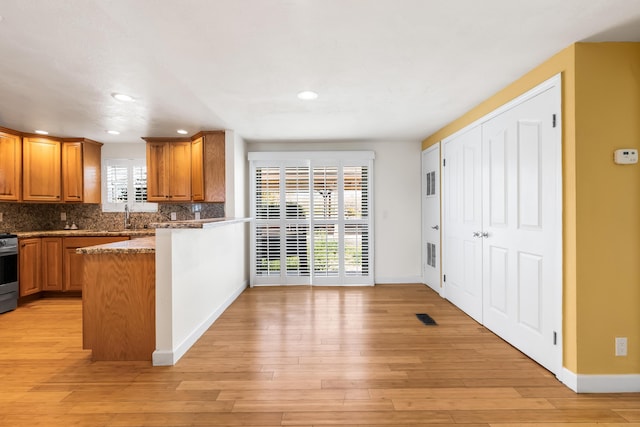 kitchen with electric range, light wood-type flooring, brown cabinets, and decorative backsplash