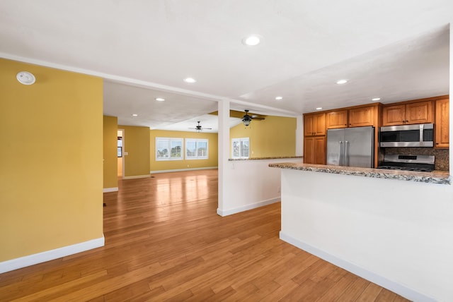 kitchen with stainless steel appliances, brown cabinetry, light wood-style flooring, and baseboards