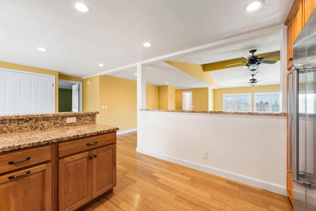 kitchen with baseboards, light stone counters, brown cabinets, light wood-type flooring, and recessed lighting