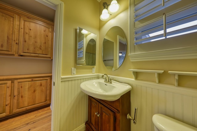 24281 Jacaranda Dr, Tehachapi, CA 93561 - bathroom with a decorative wall, toilet, wood finished floors, vanity, and wainscoting