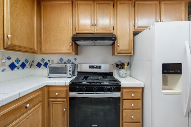 kitchen with tile countertops, gas stove, white fridge with ice dispenser, and exhaust hood