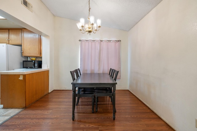 dining room with dark hardwood / wood-style flooring, lofted ceiling, a textured ceiling, and an inviting chandelier