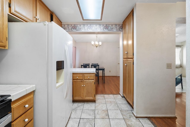 kitchen with stove, hanging light fixtures, a notable chandelier, white refrigerator with ice dispenser, and tile countertops