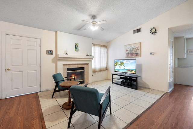 living room with lofted ceiling, a tile fireplace, ceiling fan, light hardwood / wood-style floors, and a textured ceiling