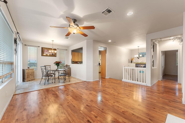 unfurnished dining area featuring ceiling fan with notable chandelier and light wood-type flooring