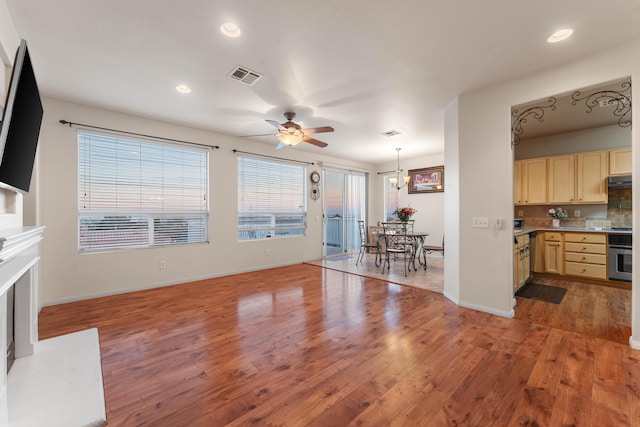 unfurnished living room featuring ceiling fan with notable chandelier and wood-type flooring