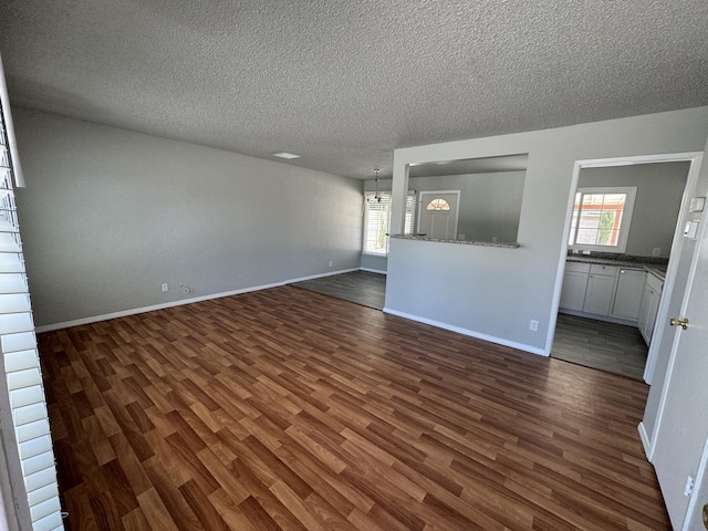 unfurnished living room featuring a chandelier, a textured ceiling, and dark hardwood / wood-style floors