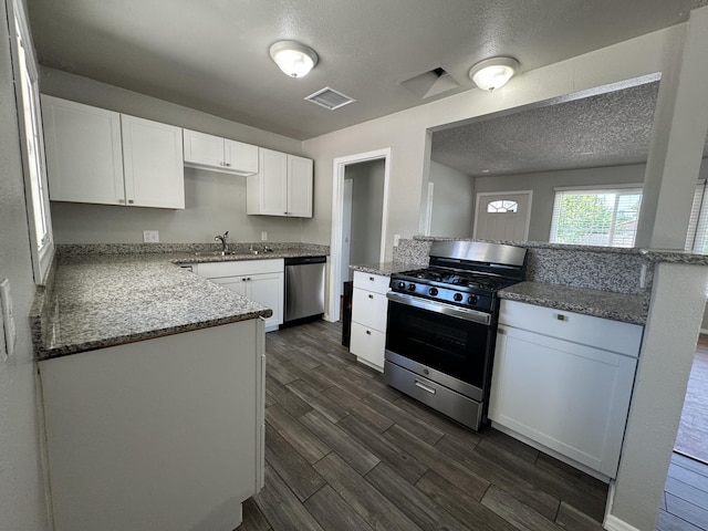 kitchen with kitchen peninsula, appliances with stainless steel finishes, light stone counters, sink, and white cabinetry