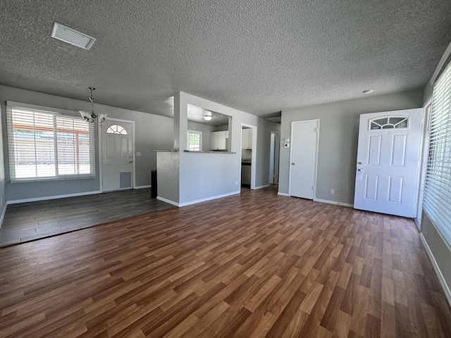 unfurnished living room with a textured ceiling, dark wood-type flooring, and an inviting chandelier