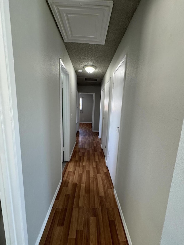 hallway with a textured ceiling and dark hardwood / wood-style floors