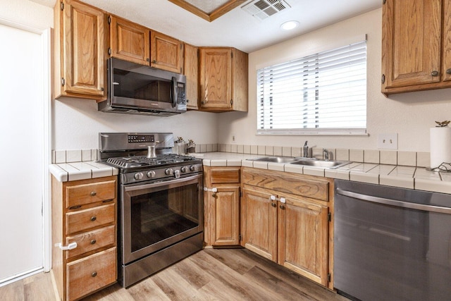 kitchen featuring stainless steel appliances, sink, tile countertops, and light wood-type flooring