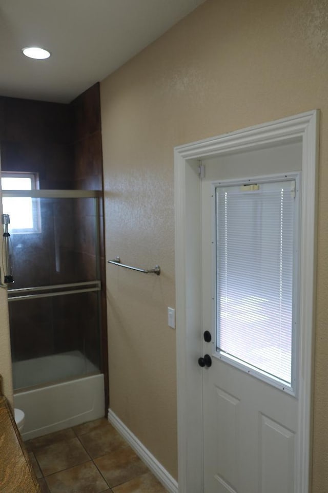 bathroom featuring tile patterned flooring, enclosed tub / shower combo, and baseboards