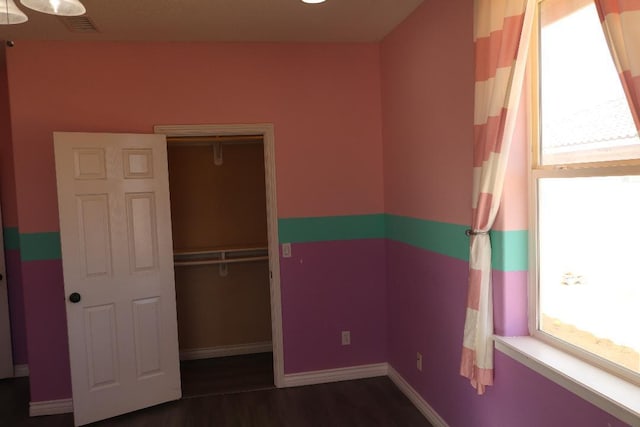 unfurnished bedroom featuring a closet, baseboards, visible vents, and dark wood-style flooring