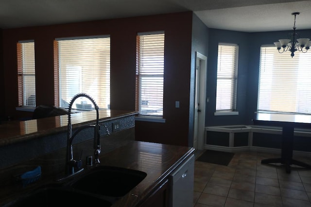 kitchen with dishwashing machine, a sink, tile patterned flooring, dark countertops, and a notable chandelier