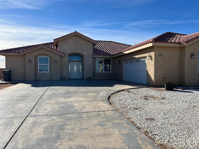 mediterranean / spanish home with a garage, driveway, a tile roof, and stucco siding