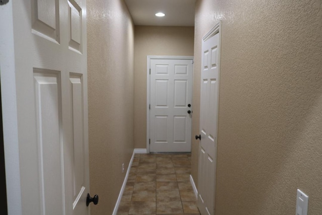 hall with tile patterned floors, baseboards, recessed lighting, and a textured wall