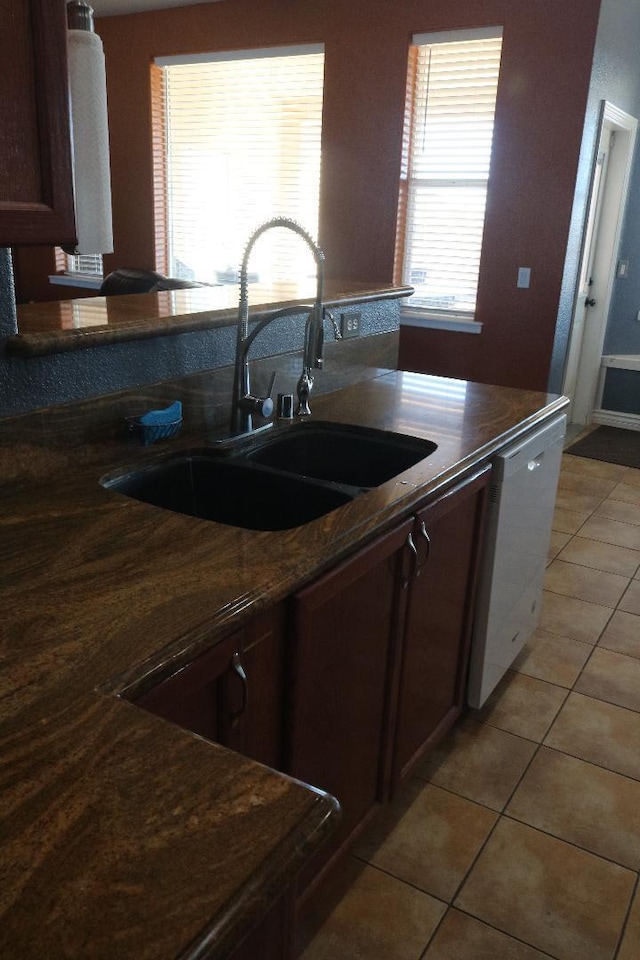 kitchen featuring light tile patterned floors, dark countertops, white dishwasher, and a sink