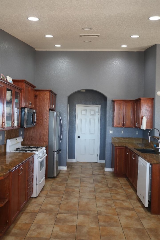 kitchen with a sink, dark countertops, appliances with stainless steel finishes, light tile patterned flooring, and a textured wall