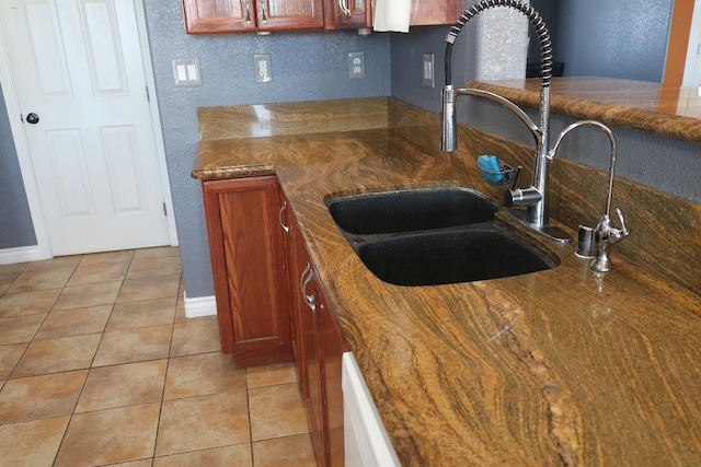 kitchen featuring light tile patterned floors, baseboards, brown cabinets, and a sink