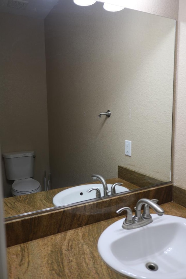 bathroom featuring a sink, visible vents, toilet, and a textured wall