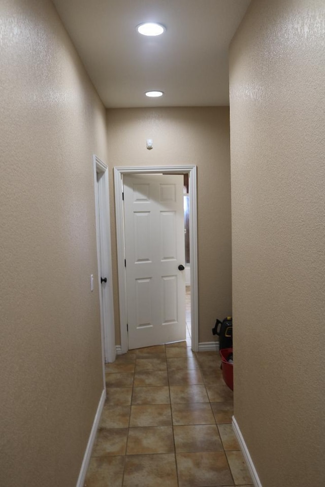 corridor featuring light tile patterned floors, a textured wall, and baseboards