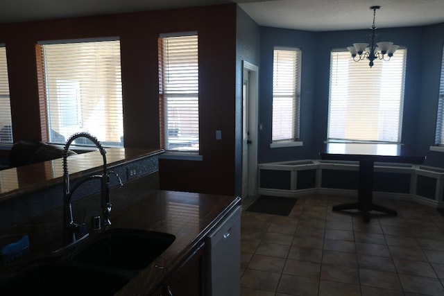 kitchen with dark tile patterned floors, a wealth of natural light, an inviting chandelier, and a sink