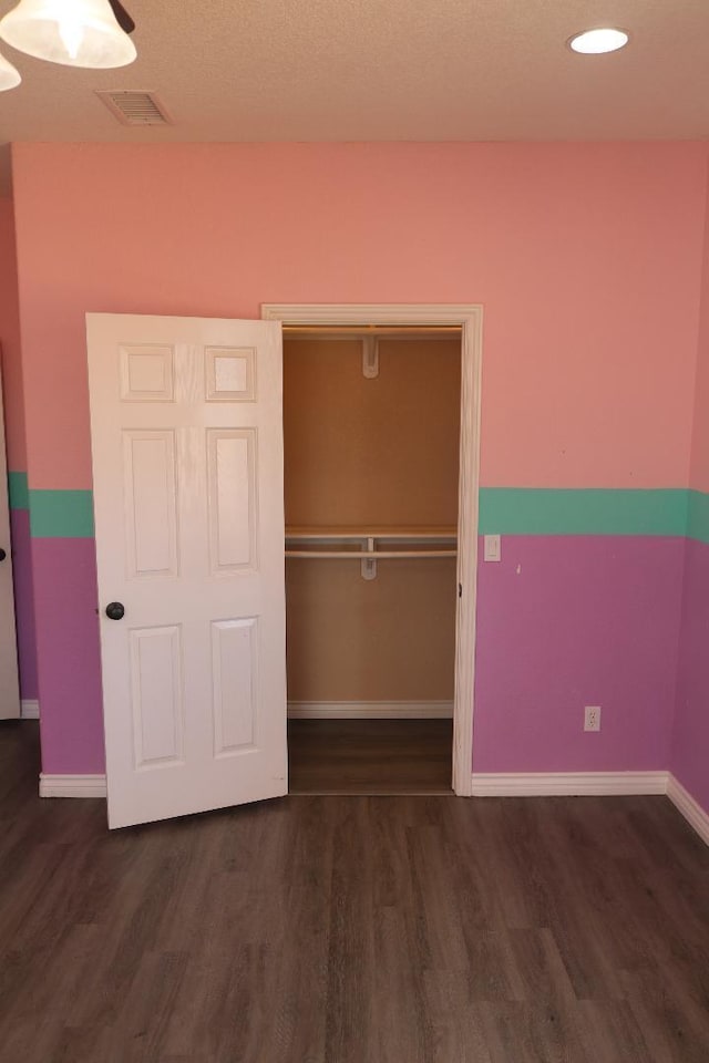 unfurnished bedroom featuring wood finished floors, visible vents, a closet, and baseboards