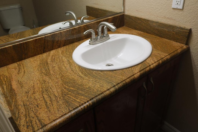 bathroom featuring toilet, vanity, and a textured wall