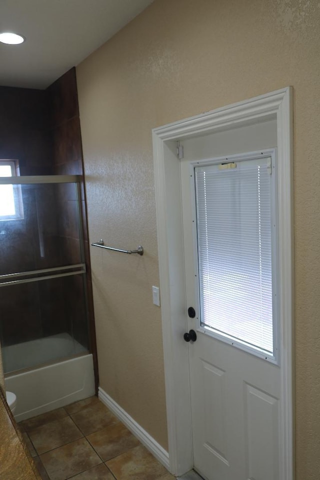 bathroom with tile patterned floors, baseboards, and bath / shower combo with glass door