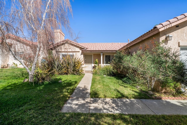 view of front of house featuring a tile roof, a chimney, a front lawn, and stucco siding