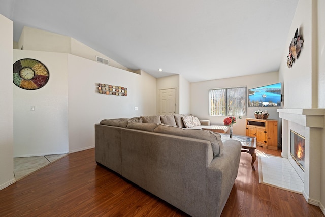 living room with lofted ceiling, a glass covered fireplace, wood finished floors, and visible vents