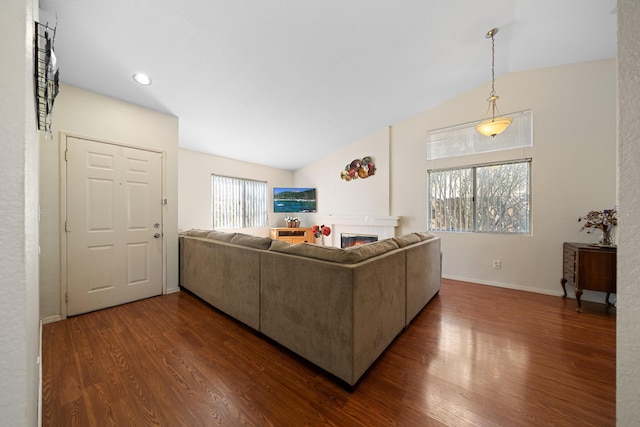 living area with lofted ceiling, dark wood-type flooring, a glass covered fireplace, and baseboards