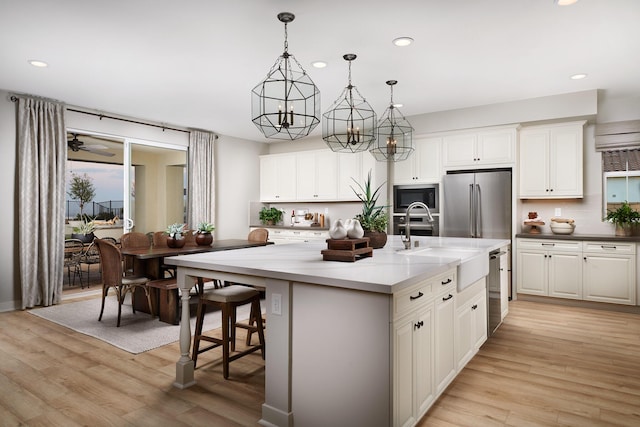 kitchen featuring tasteful backsplash, stainless steel appliances, an island with sink, and light wood-style floors