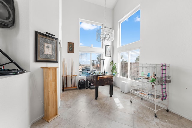 recreation room with a towering ceiling, light tile patterned flooring, and a notable chandelier