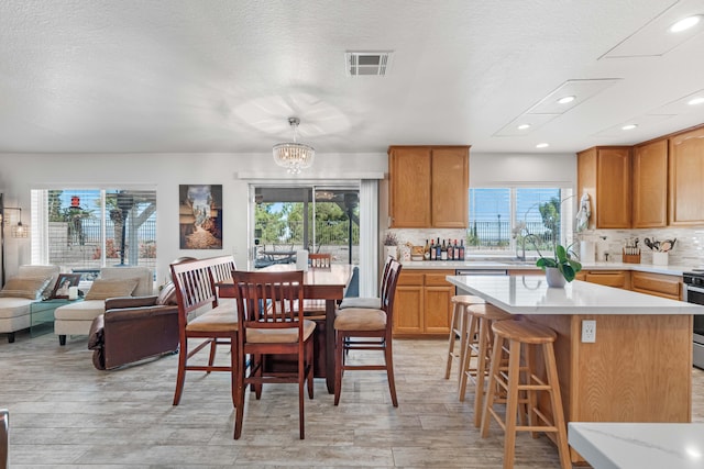 kitchen with an inviting chandelier, a kitchen breakfast bar, decorative light fixtures, stainless steel range oven, and decorative backsplash