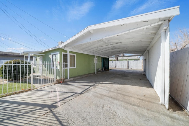 view of vehicle parking featuring an attached carport, fence, and concrete driveway