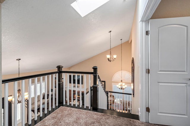 hallway featuring lofted ceiling with skylight, an upstairs landing, and an inviting chandelier
