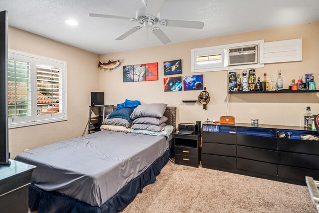 bedroom with a ceiling fan, light colored carpet, a wall unit AC, and a textured ceiling