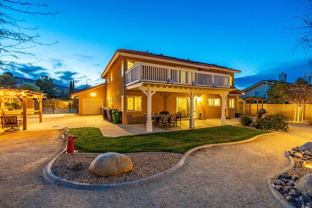 back of property at dusk with stucco siding, fence, an attached garage, and a patio