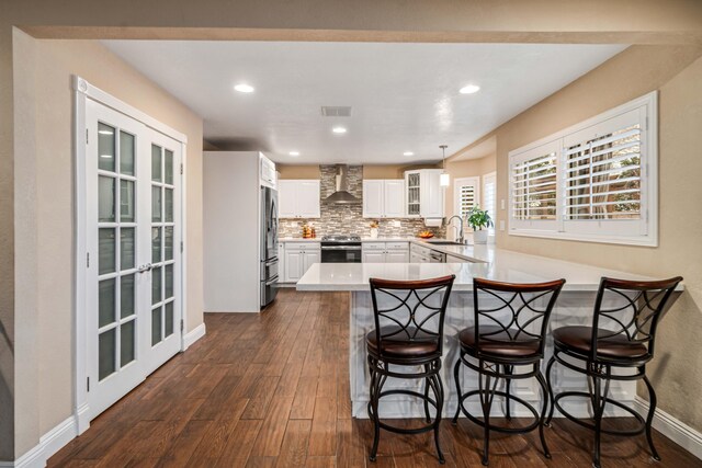 kitchen with dark wood finished floors, a peninsula, stainless steel appliances, wall chimney range hood, and a sink