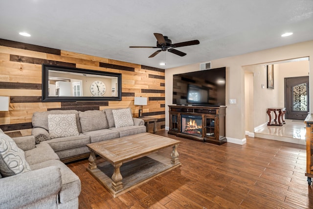living area with baseboards, a glass covered fireplace, wood finished floors, wood walls, and recessed lighting